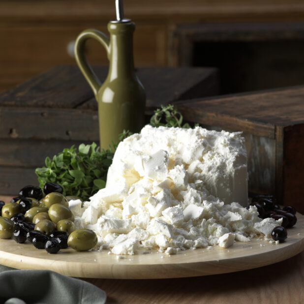 A Wooden Platter of Freshly Crumbled Feta Cheese and Marinated Green and Black Olives on a Wooden Surface in an Indoor Setting