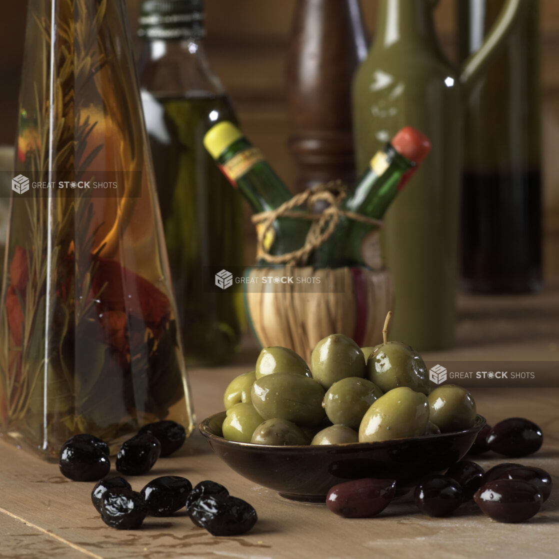 Marinated Green, Black and Kalamata Olives on a Wooden Table with a Bottle of Herbed Olive Oil in a Kitchen Setting