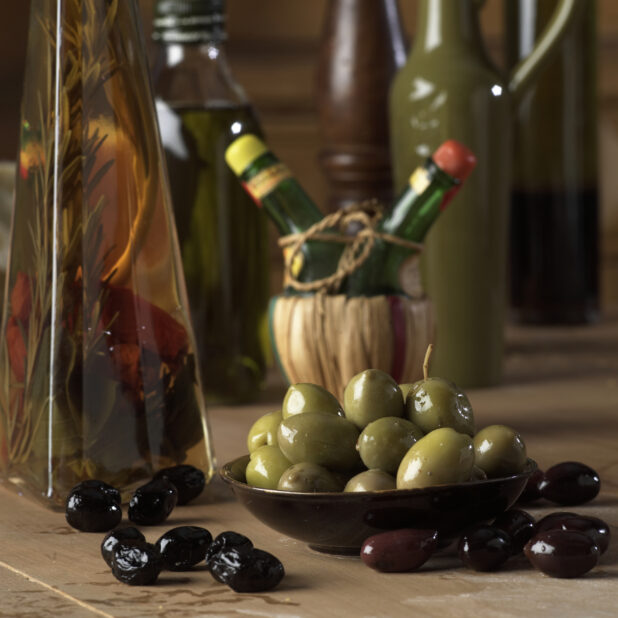 Marinated Green, Black and Kalamata Olives on a Wooden Table with a Bottle of Herbed Olive Oil in a Kitchen Setting