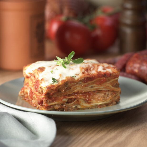 Thick Stacked Meat Lasagna on a Grey Ceramic Dish on a Wooden Table in an Indoor Setting