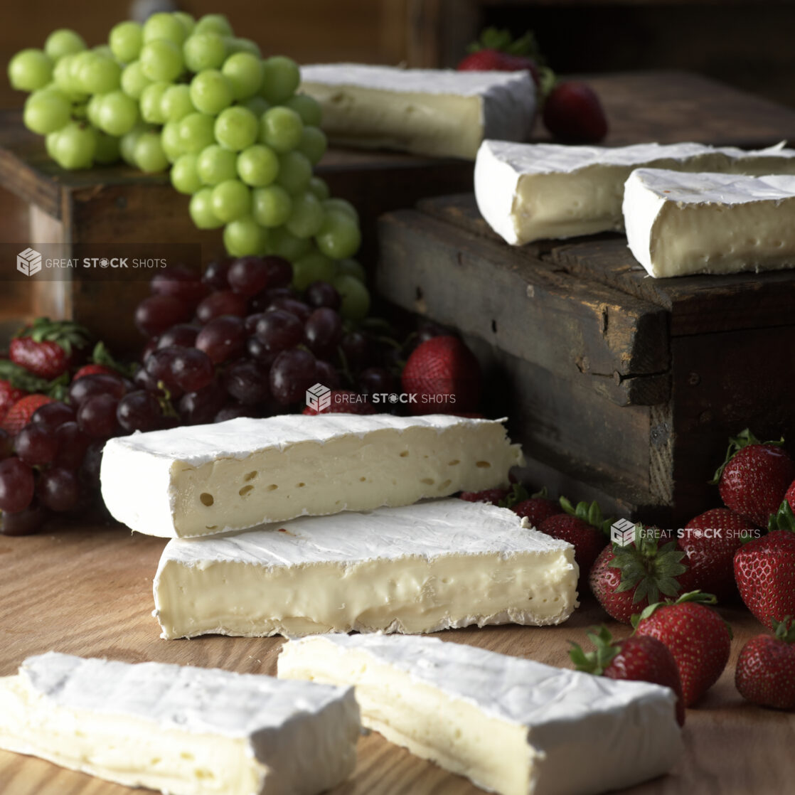 Wedges of Creamy Brie Cheese with Fresh Strawberries and Grapes on a Wooden Table in a Kitchen Setting