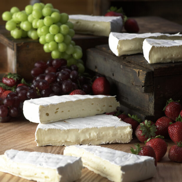 Wedges of Creamy Brie Cheese with Fresh Strawberries and Grapes on a Wooden Table in a Kitchen Setting