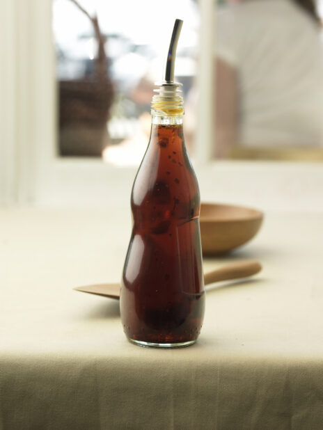 Glass Bottle with a Drizzle Spout and Salad Dressing on a Table Cloth Surface in an Indoor Setting