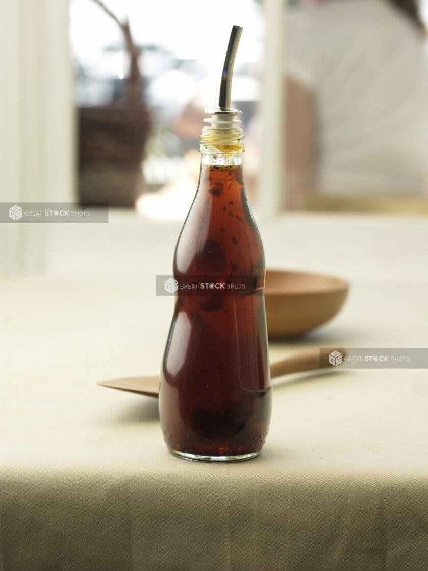 Glass Bottle with a Drizzle Spout and Salad Dressing on a Table Cloth Surface in an Indoor Setting