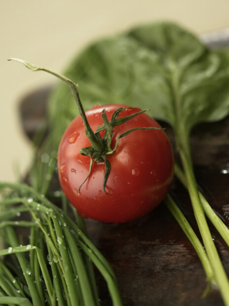 Close Up of a Whole Vine-Ripened Tomato with Fresh Spinach Leaves and Green Spring Onions on a Dark Wooden Platter