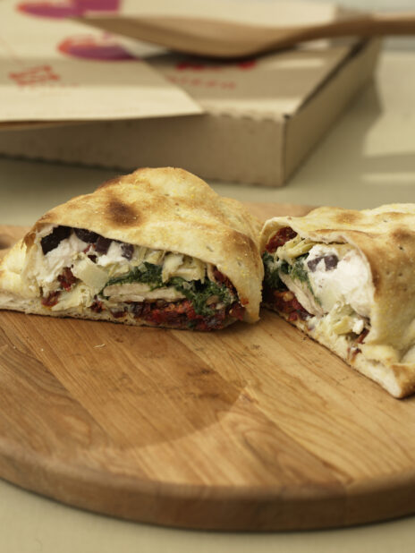 Cut Calzone with Spinach, Ricotta, Sun-dried Tomatoes, Black Olives and Artichoke Hearts Stuffing on a Wooden Pizza Peel