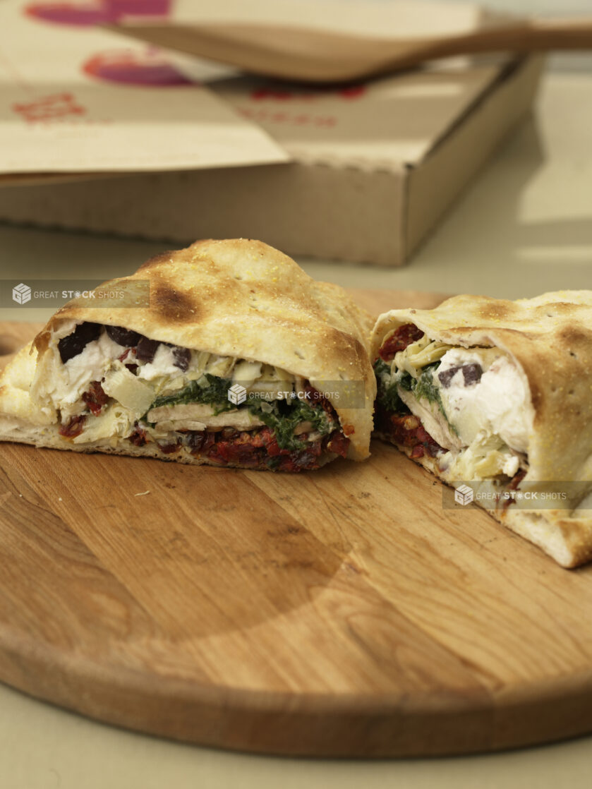 Cut Calzone with Spinach, Ricotta, Sun-dried Tomatoes, Black Olives and Artichoke Hearts Stuffing on a Wooden Pizza Peel