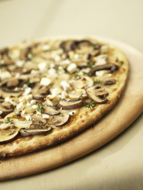 Close Up of a New York-Style Mushroom Pizza on a Wooden Pizza Peel in an Indoor Setting