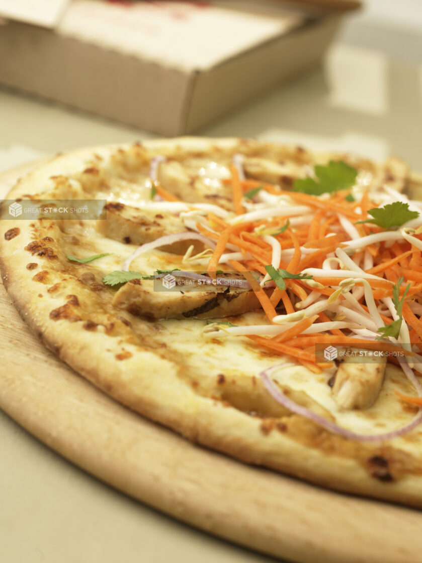 Close Up of a New York-Style Pizza with Asian Sesame Chicken and Vegetable Toppings on a Wooden Pizza Peel in an Indoor Setting