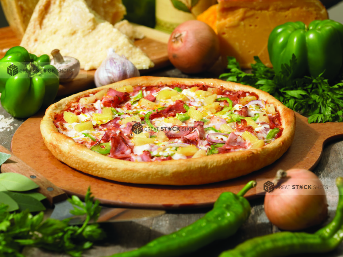 Gourmet Thick Crust Hawaiian Pizza with Sliced Vegetables, Ham and Pineapple on a Wooden Pizza Peel in an Indoor Setting