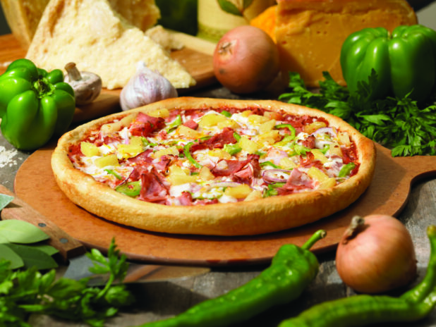 Gourmet Thick Crust Hawaiian Pizza with Sliced Vegetables, Ham and Pineapple on a Wooden Pizza Peel in an Indoor Setting