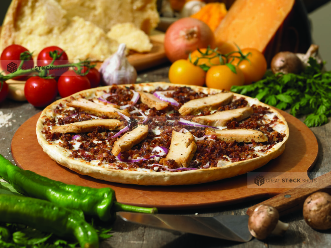 Whole Thin Crust Pizza with Grilled Chicken Strips, Ground Beef and Sliced Red Onions on a Wooden Pizza Peel in an Indoor Setting