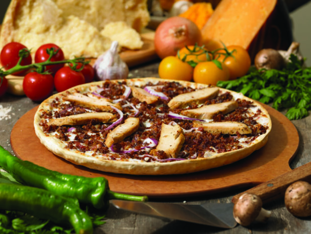 Whole Thin Crust Pizza with Grilled Chicken Strips, Ground Beef and Sliced Red Onions on a Wooden Pizza Peel in an Indoor Setting