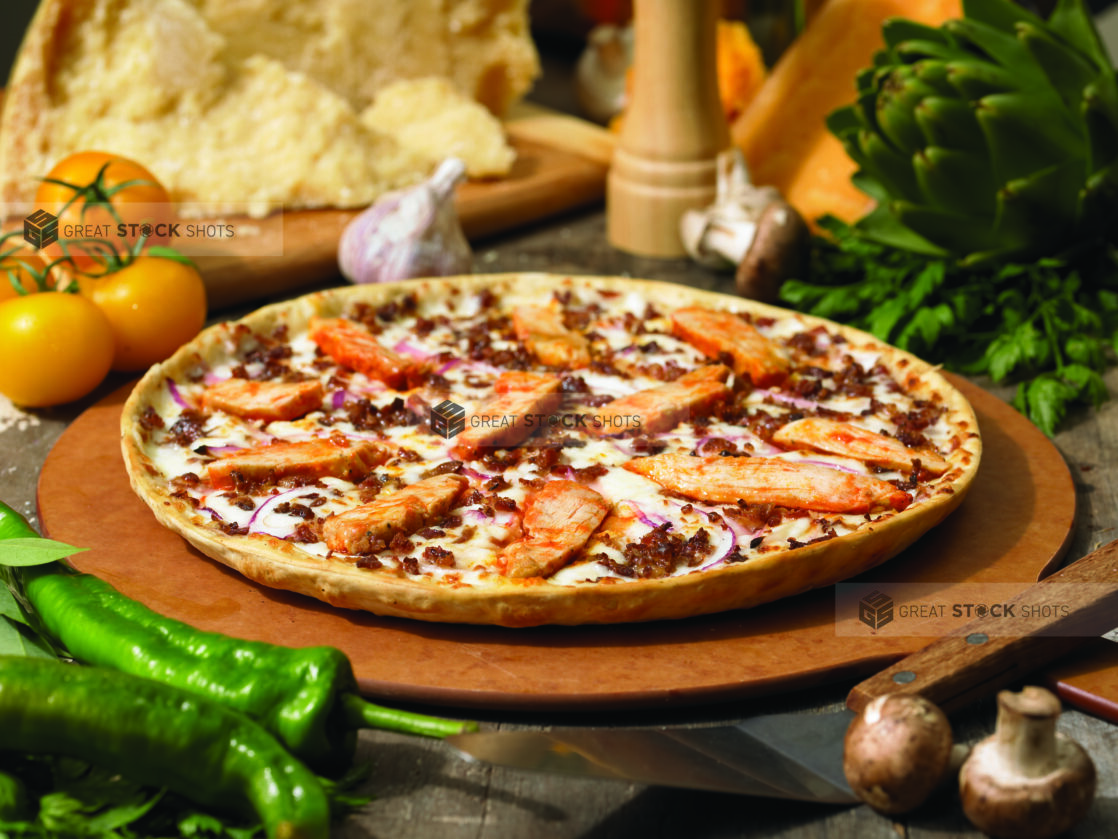 Whole Thin Crust Pizza with BBQ Chicken, Ground Beef and Sliced Red Onions on a Wooden Pizza Peel in an Indoor Setting