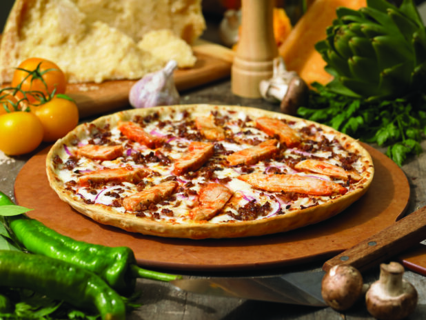 Whole Thin Crust Pizza with BBQ Chicken, Ground Beef and Sliced Red Onions on a Wooden Pizza Peel in an Indoor Setting