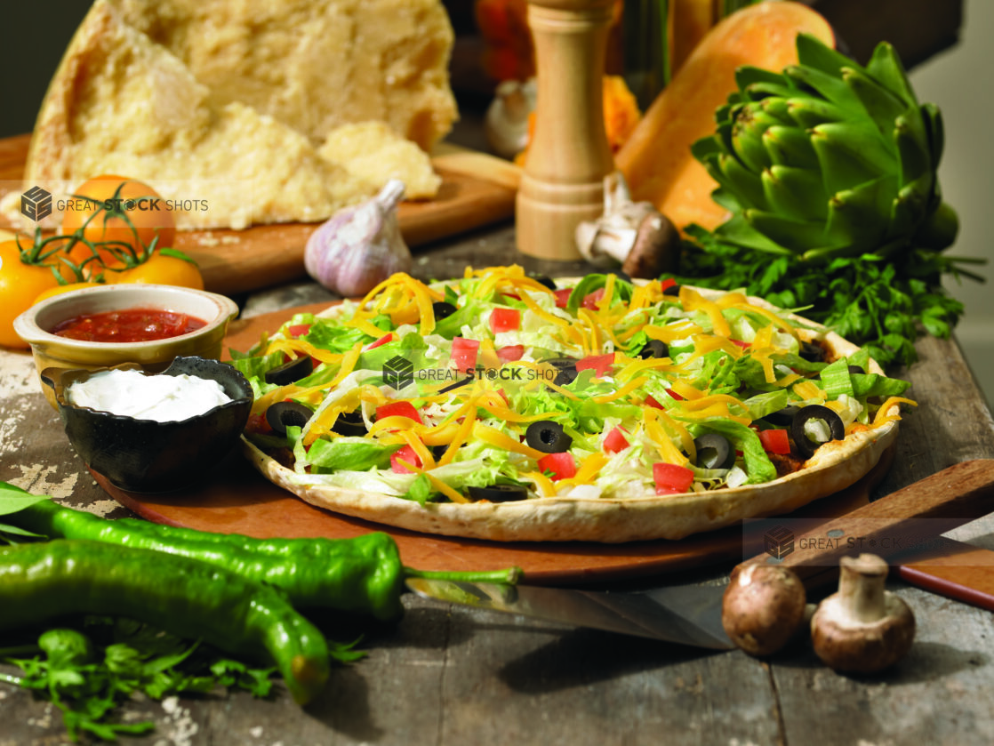 Tex-Mex Taco or Nacho Pizza with Side Bowls of Sour Cream and Salsa on a Wooden Pizza Peel in an Indoor Setting