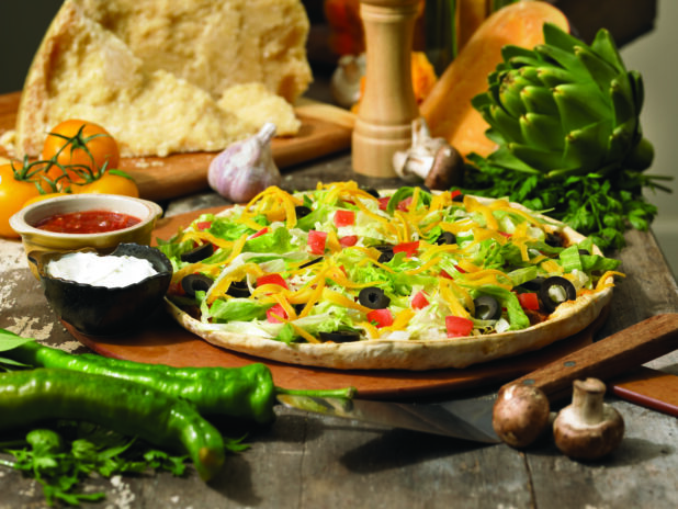 Tex-Mex Taco or Nacho Pizza with Side Bowls of Sour Cream and Salsa on a Wooden Pizza Peel in an Indoor Setting