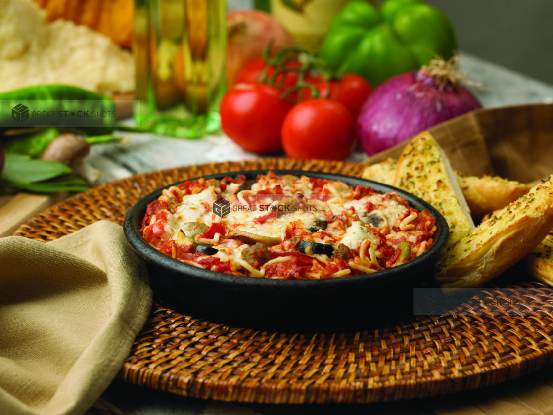 Baked Vegetables and Spaghetti in a Cast Iron Skillet with a Side of Garlic Bread on a Woven Placemat