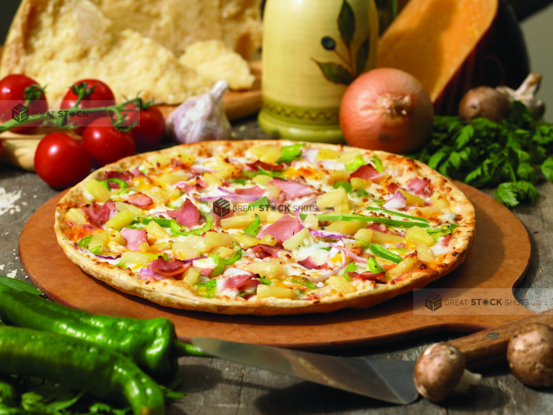 Gourmet Thin Crust Hawaiian Pizza with Sliced Vegetables, Ham and Pineapple on a Wooden Pizza Peel in an Indoor Setting