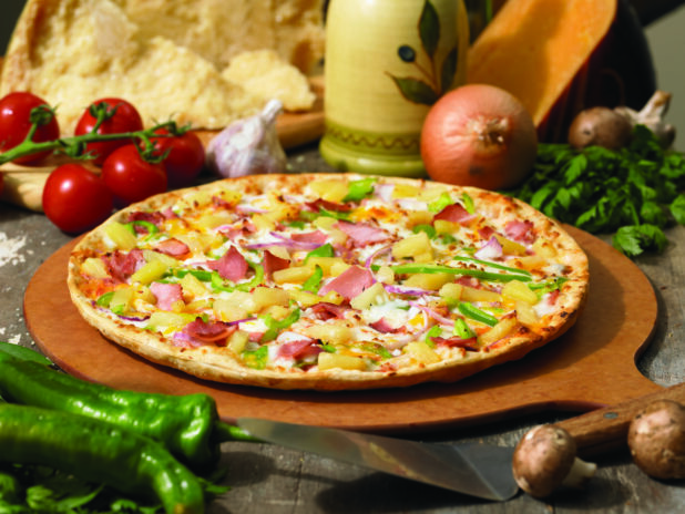 Gourmet Thin Crust Hawaiian Pizza with Sliced Vegetables, Ham and Pineapple on a Wooden Pizza Peel in an Indoor Setting