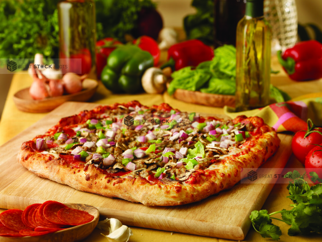 A Square Personal Pizza with Diced Vegetables in Italian Sausage Crumble on a Wooden Cutting Board in an Indoor Setting