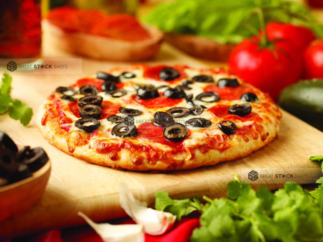 A Personal-Sized Pepperoni and Black Olives Pizza on a Wooden Cutting Board in an Indoor Setting