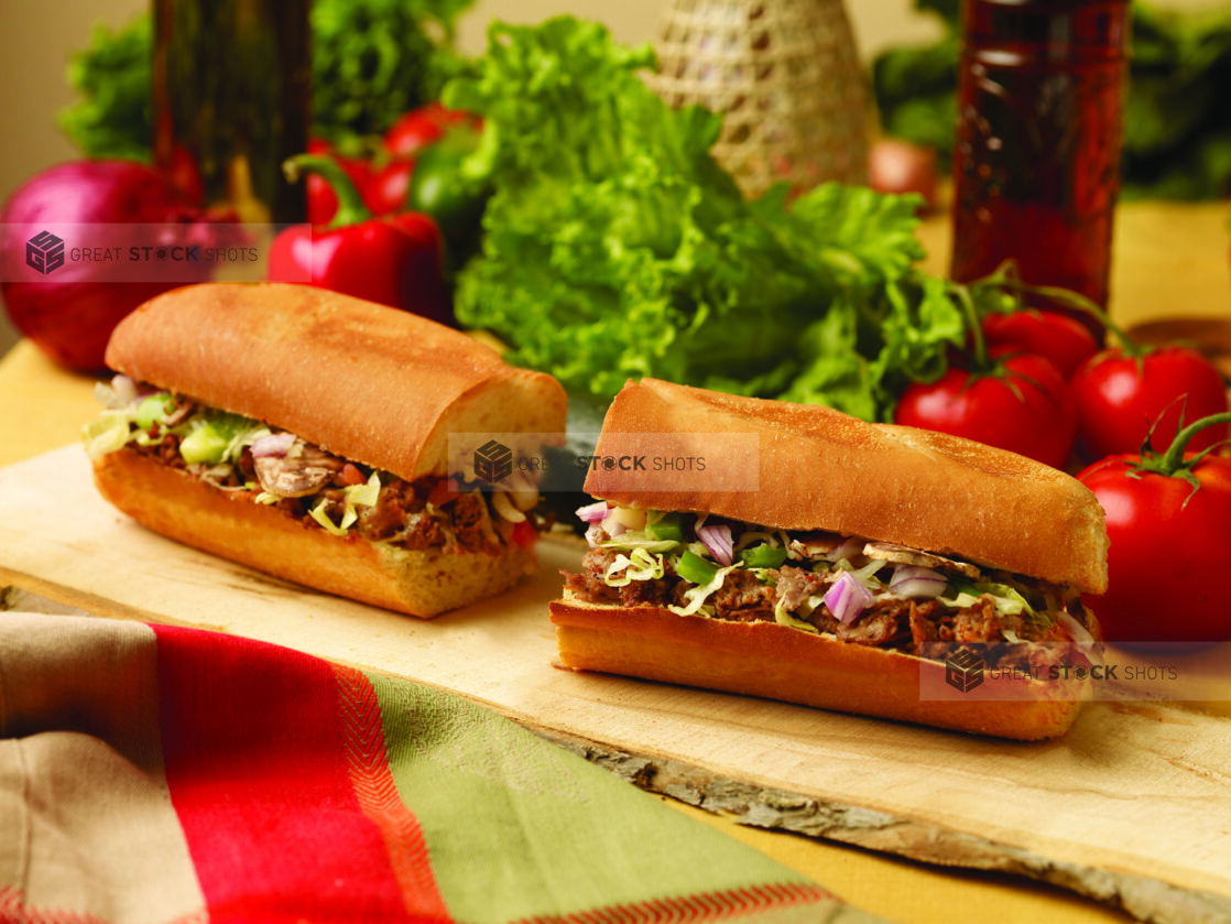 A Cheesesteak Sub Sandwich Cut in Half on a Wooden Platter in an Indoor Setting