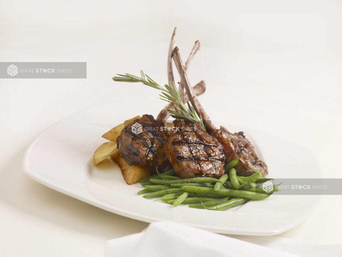 Agnello Scottadito - Italian Lamb Chops - with Green Beans and Potato Wedges on a White Ceramic Dish