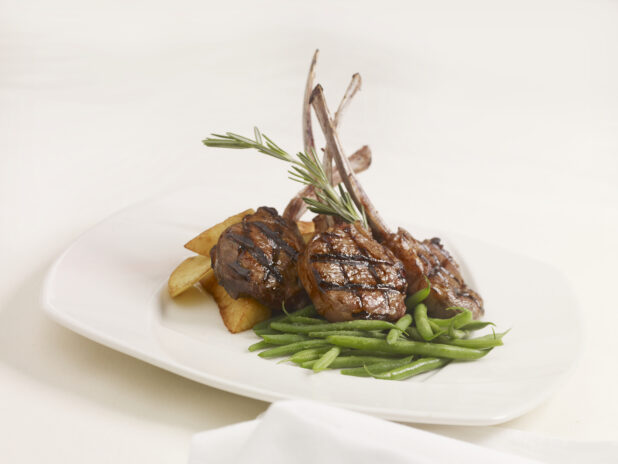 Agnello Scottadito - Italian Lamb Chops - with Green Beans and Potato Wedges on a White Ceramic Dish