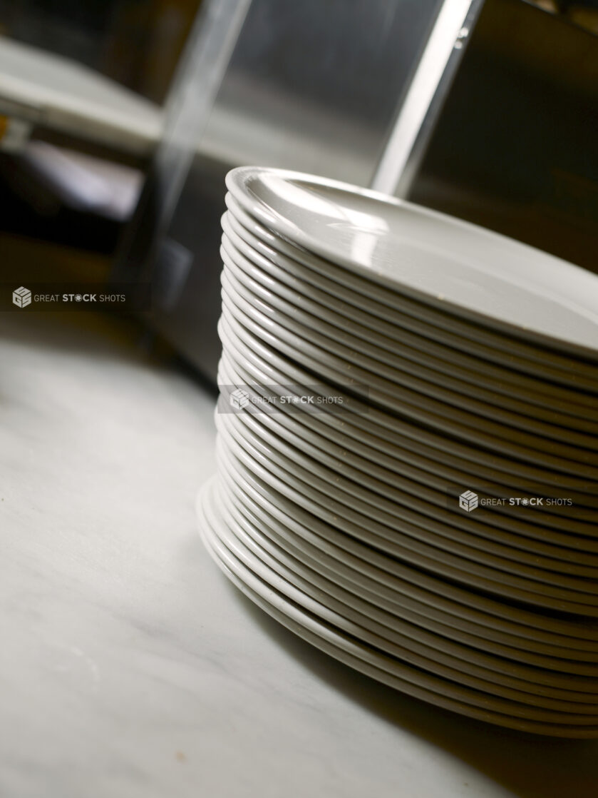 A Stack of White Ceramic Dinner Plates on a White Marble Countertop in a Commercial Kitchen Setting