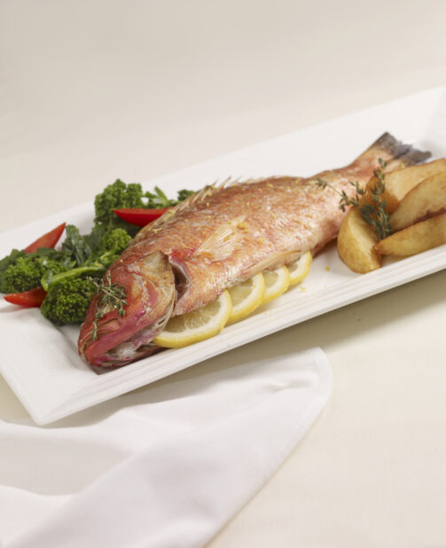 Baked Whole Red Snapper with Citrus and Herbs, Rapini and Potato Wedges on a White Ceramic Dish