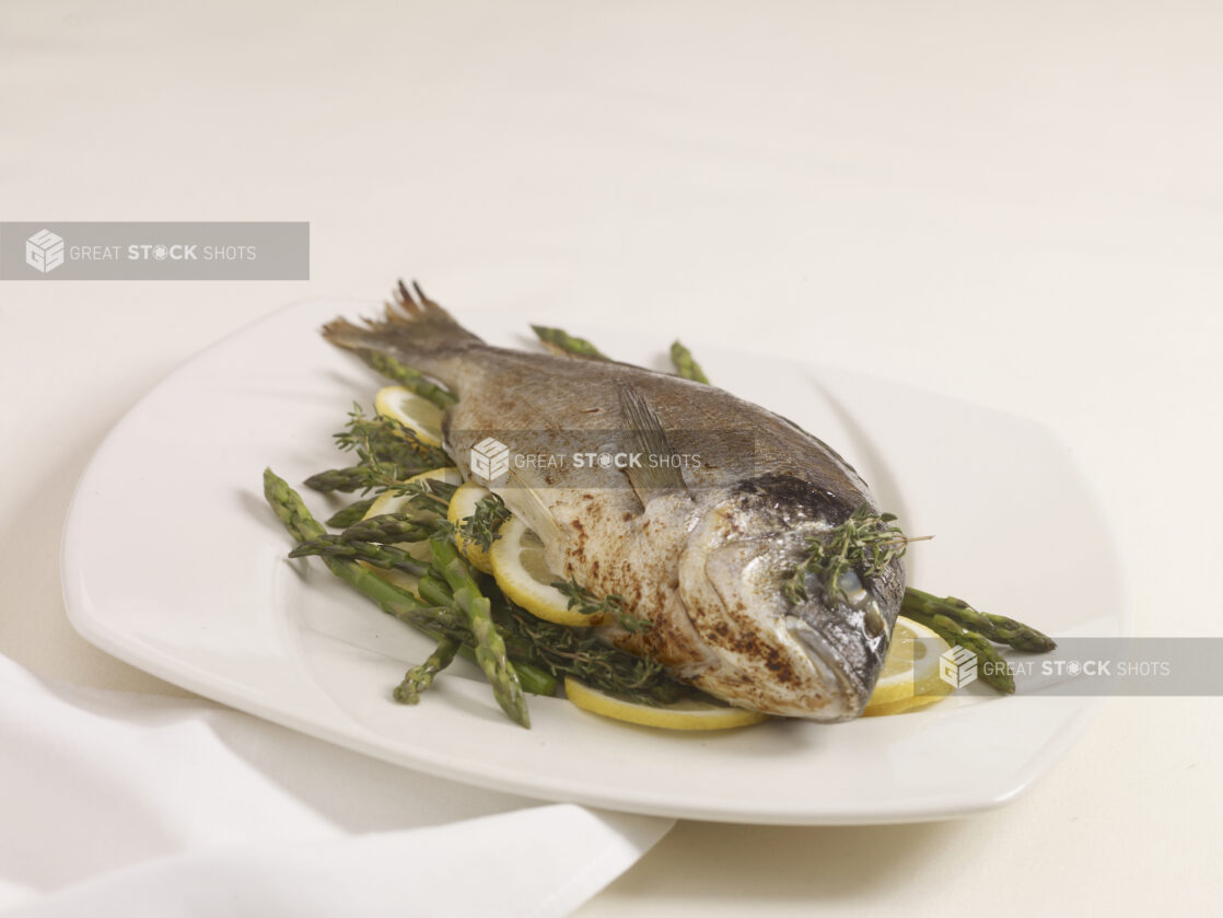 A Whole Roasted Sea Bream with Asparagus, Citrus and Herbs on a White Ceramic Dish