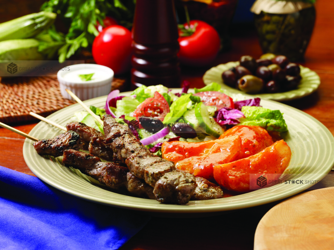 A Combo Plate of Pork Souvlaki, Greek Salad and Roasted Greek Potatoes on a Beige Ceramic Dish on a Wooden Table