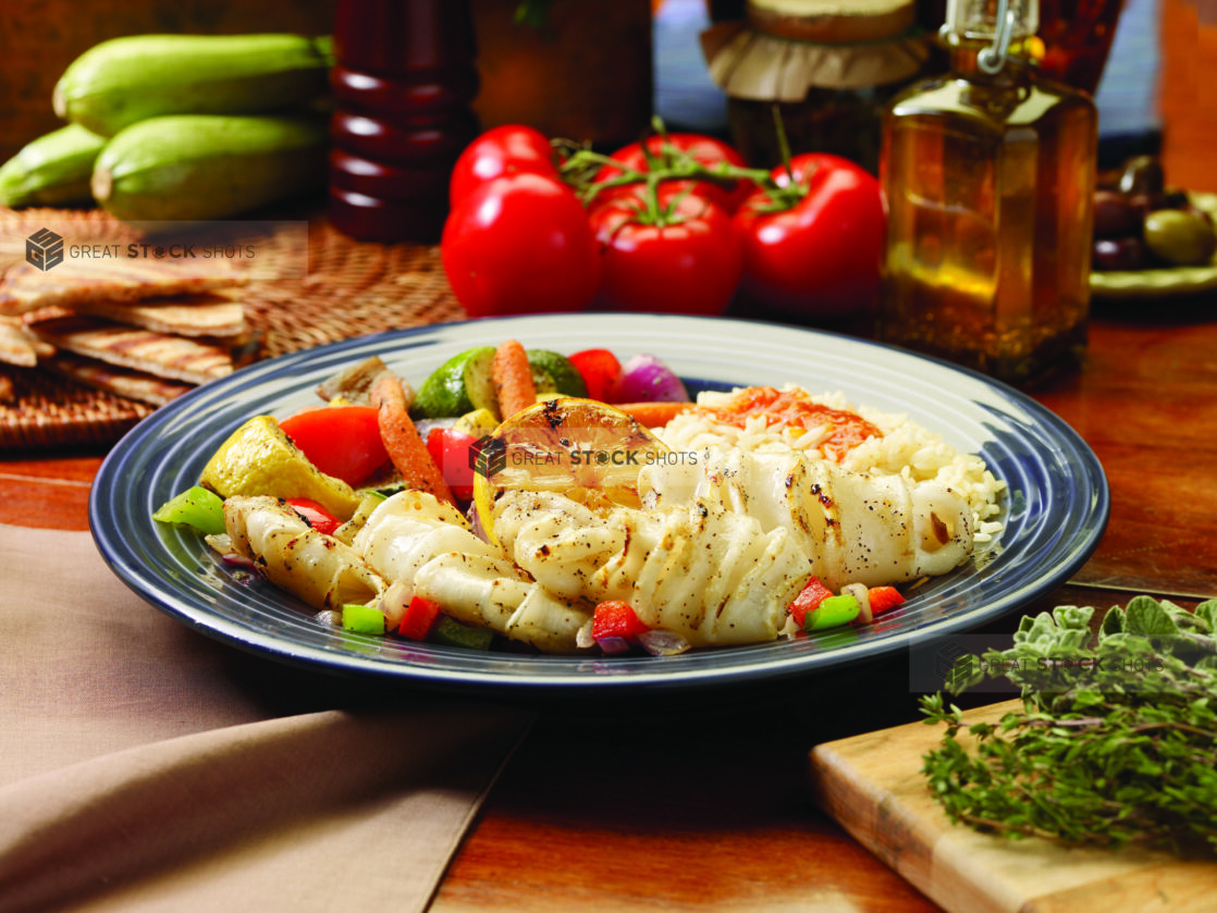 A Combo Plate of Grilled Calamari, Roasted Vegetables and White Rice on a Blue Ceramic Dish on a Wooden Table