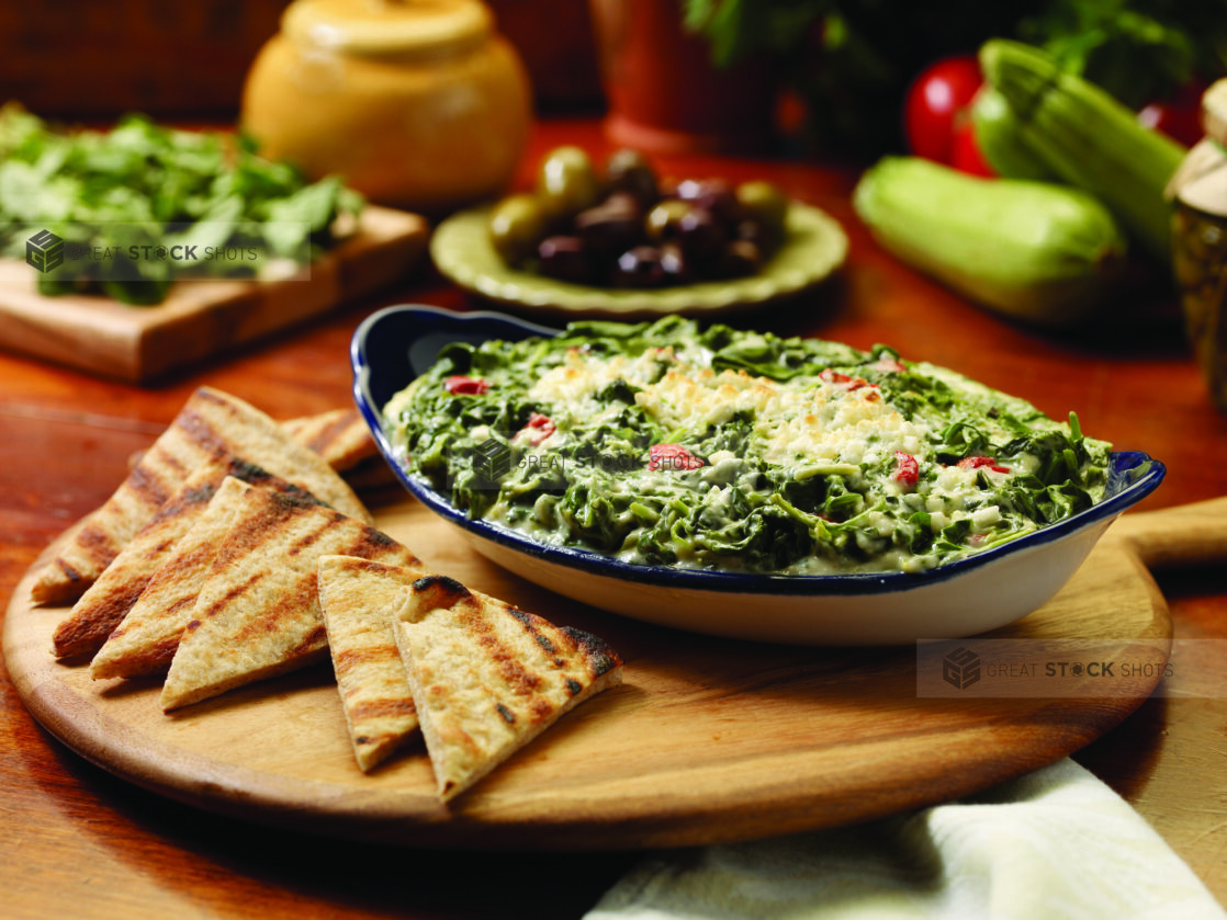 Spanakopita Dip (Greek Spinach and Cheese Dip) with Grilled Pita Bread Wedges on a Wooden Platter on a Wooden Table