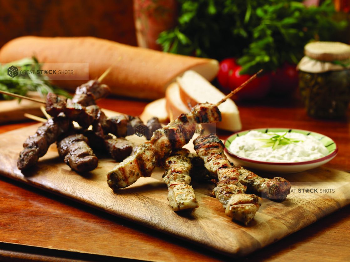 Wooden Platter of Mini Pork and Chicken Souvlaki with a Side of Tzatziki Sauce on a Wooden Table