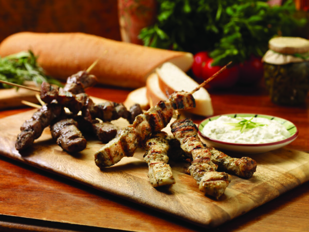 Wooden Platter of Mini Pork and Chicken Souvlaki with a Side of Tzatziki Sauce on a Wooden Table