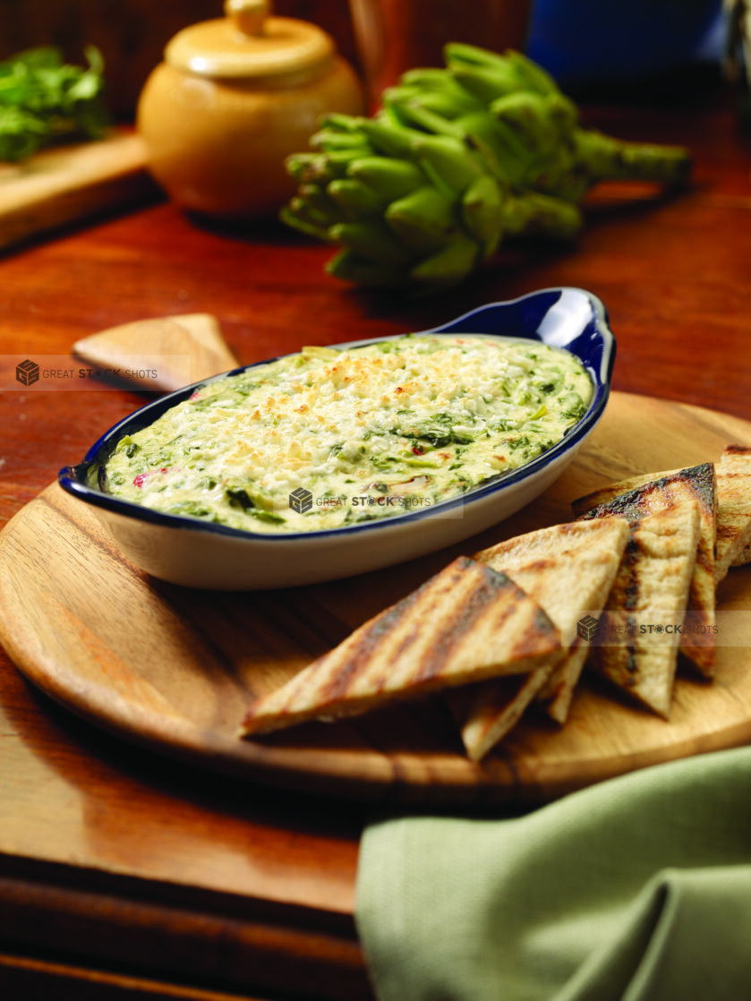 Spanakopita Dip (Greek Spinach and Cheese Dip) with Grilled Pita Bread Wedges on a Wooden Platter on a Wooden Table - Variation