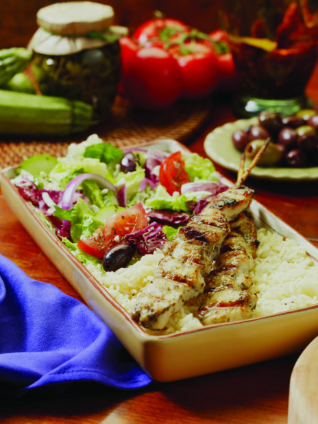 A Combo Plate of Chicken Souvlaki, Greek Salad and White Rice in a Rectangular Ceramic Dish on a Wooden Table