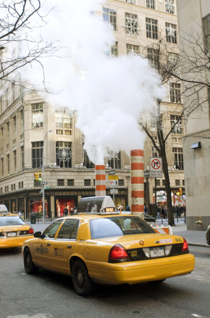 Yellow NYC Taxi Cabs Passing Large Steam Pipe Vent Stacks on the Streets of Manhattan, New York City During Winter
