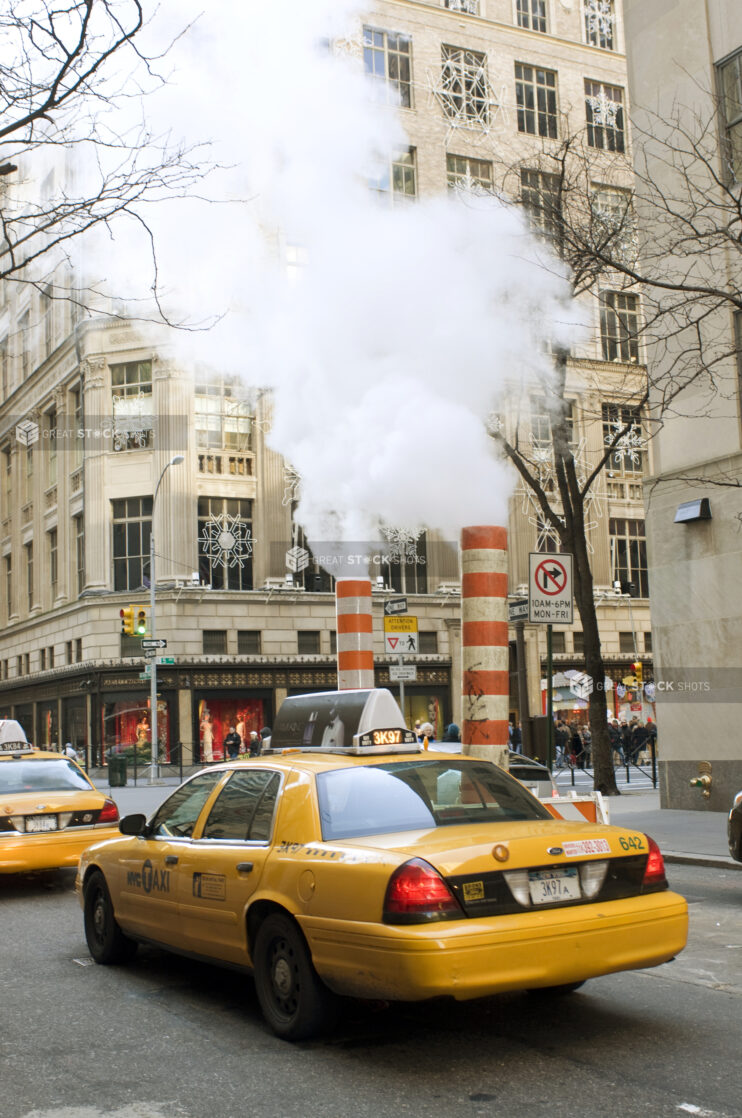 Yellow NYC Taxi Cabs Passing Large Steam Pipe Vent Stacks on the Streets of Manhattan, New York City During Winter