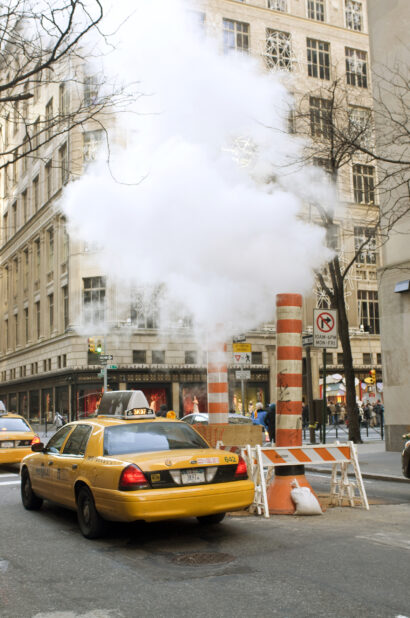 Yellow NYC Taxi Cabs Passing Large Steam Pipe Vent Stacks on the Streets of Manhattan, New York City During Winter - Variation