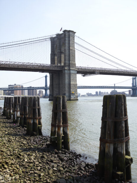 View of the Brooklyn Bridge from the Pebble Beach Shore of the East River with Mooring Posts in the Foreground in Manhattan, New York City