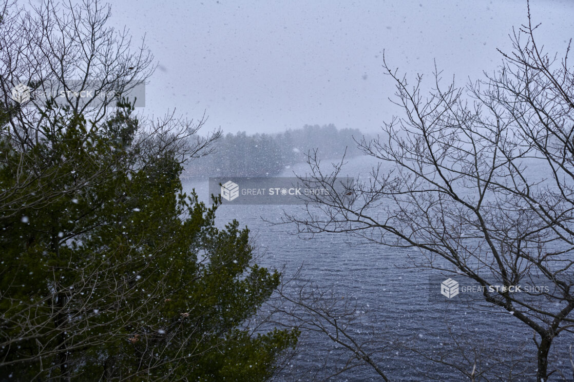 Aerial View Through Trees of a Lake During Winter with Flurries in Cottage Country, Ontario, Canada