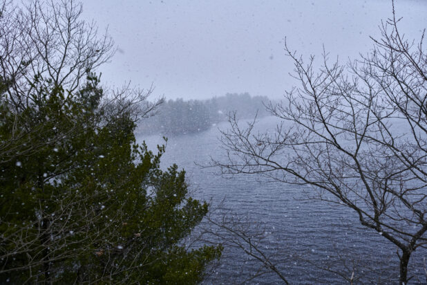 Aerial View Through Trees of a Lake During Winter with Flurries in Cottage Country, Ontario, Canada