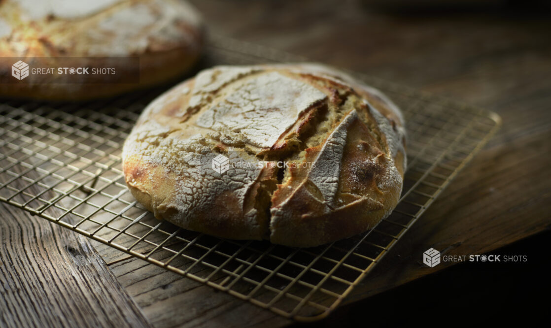 Close Up of a Round Loaf of Sourdough Bread Cooling on a Wire Rack on a Rustic Wooden Table in an Indoor Setting