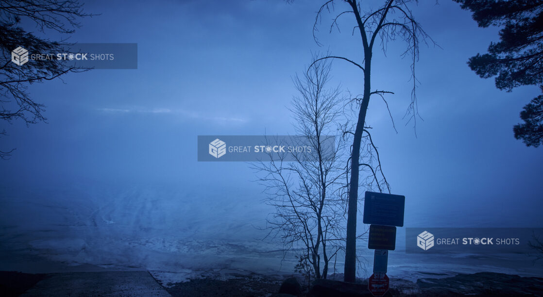 Warning Signs and Bare Trees on a Hill Overlooking a Frozen Ice-Covered Lake in Cottage Country in Ontario, Canada