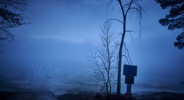 Warning Signs and Bare Trees on a Hill Overlooking a Frozen Ice-Covered Lake in Cottage Country in Ontario, Canada
