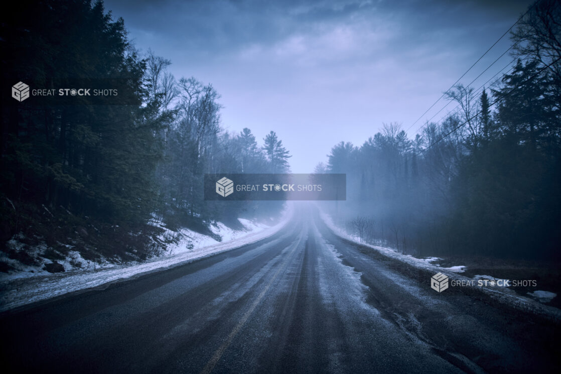 View Down a Snowy, Pine Tree-Lined Empty Road During Winter in Cottage Country, Ontario, Canada