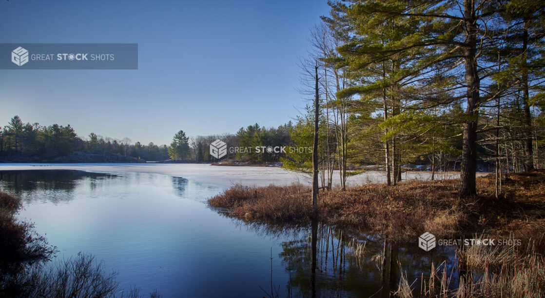 Partially Frozen Lake Surrounded by a Forest of Evergreens at Sunset in Cottage Country in Ontario, Canada